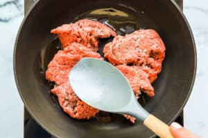 Pressing uncooked ground beef into a pan.