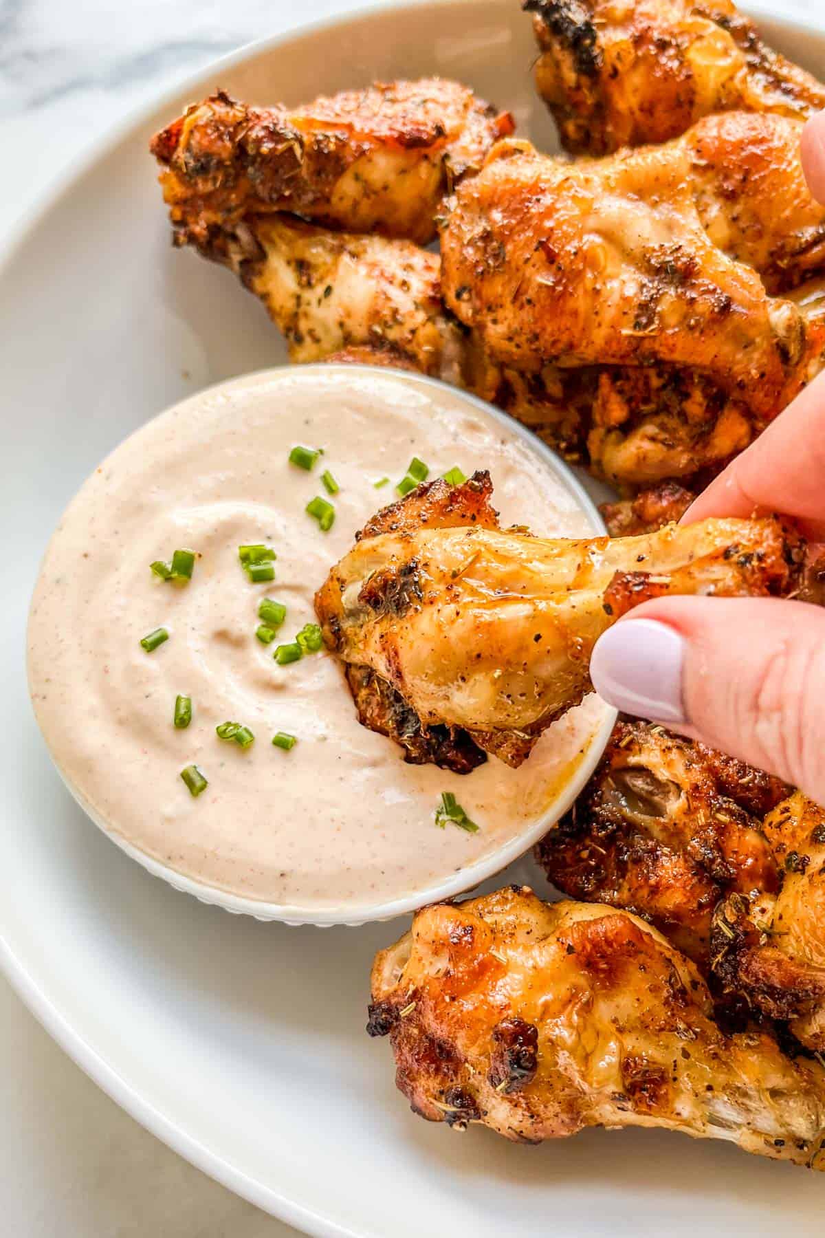 A chicken wing being dipped into sauce.