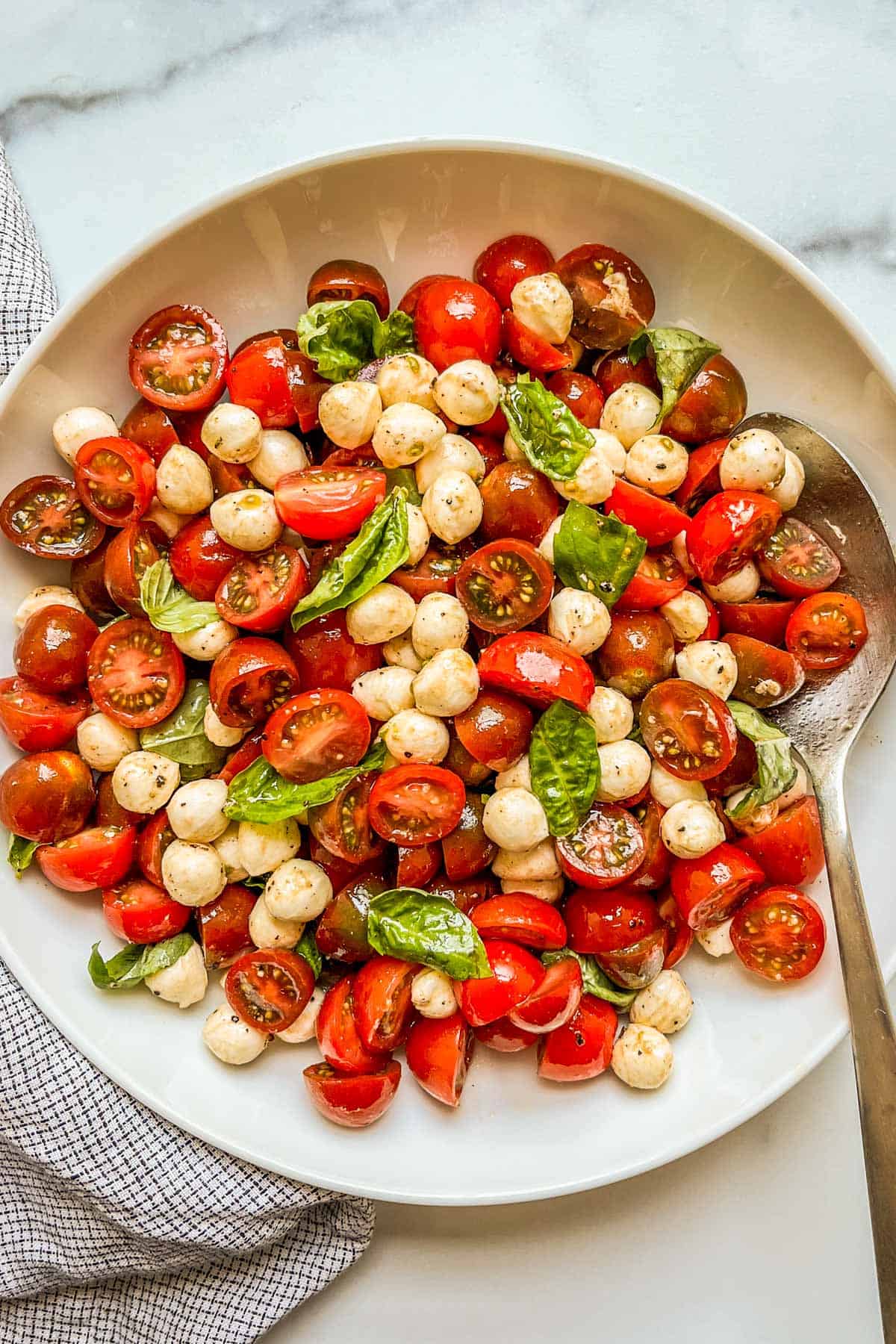 Cherry tomato caprese salad in a white bowl with a silver spoon.