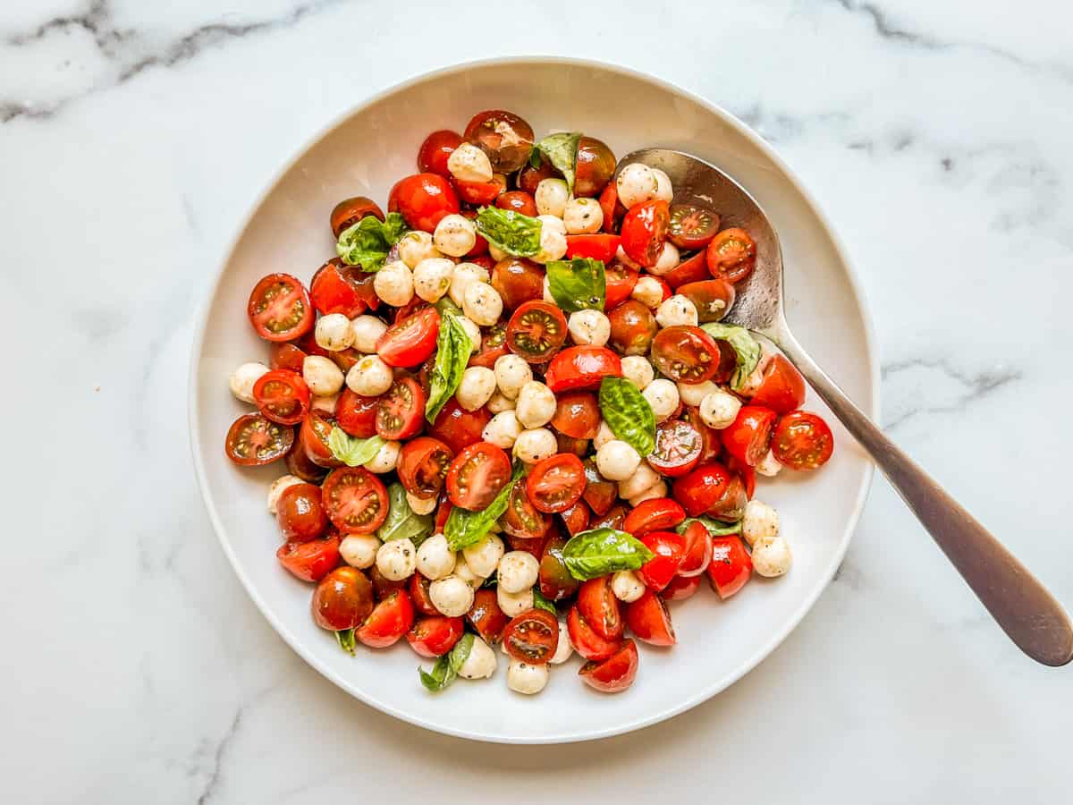 A large white serving bowl with cherry tomato caprese salad.