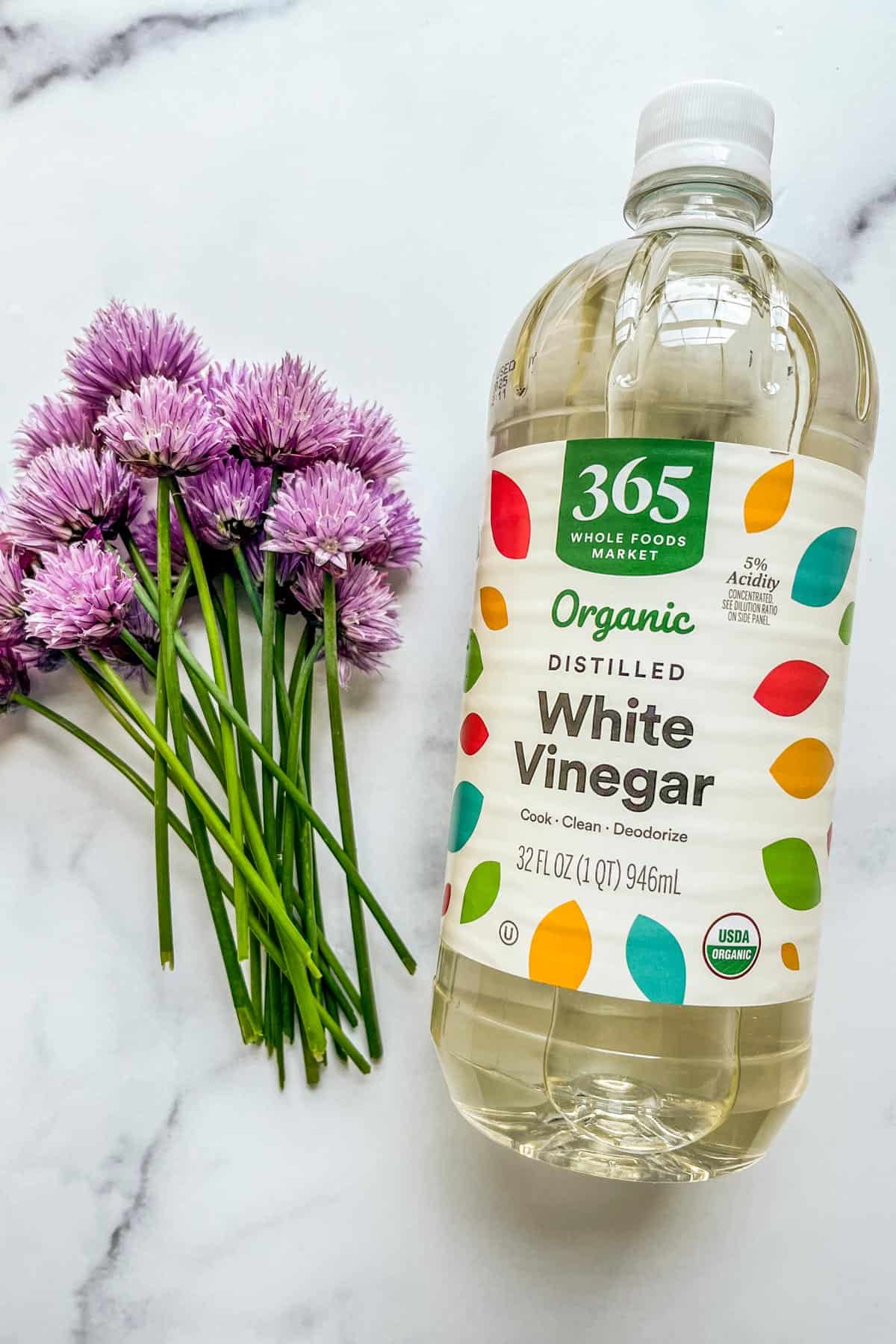 A bottle of white vinegar and a bunch of chive blossoms.