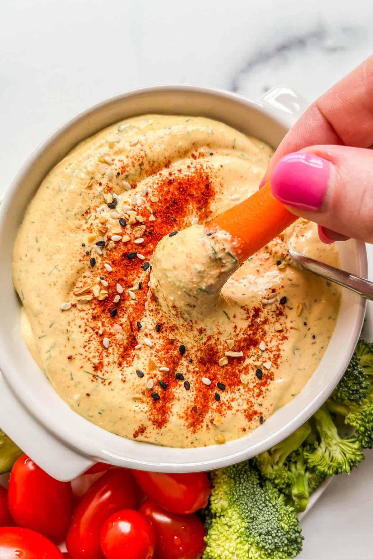 A baby carrot being dipped into a blend of cottage cheese and mustard.