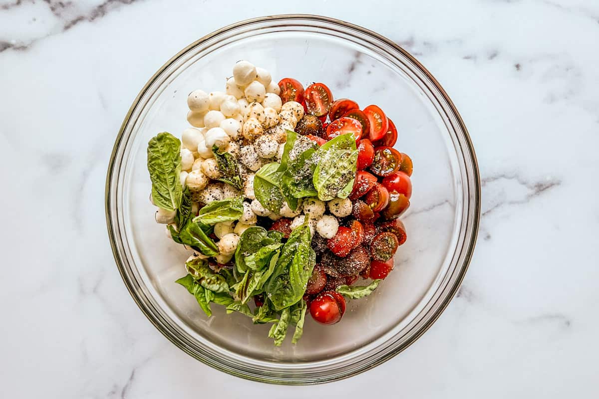 Cherry tomatoes, basil, pearl mozzarella balls, sald, and pepper in a bowl.