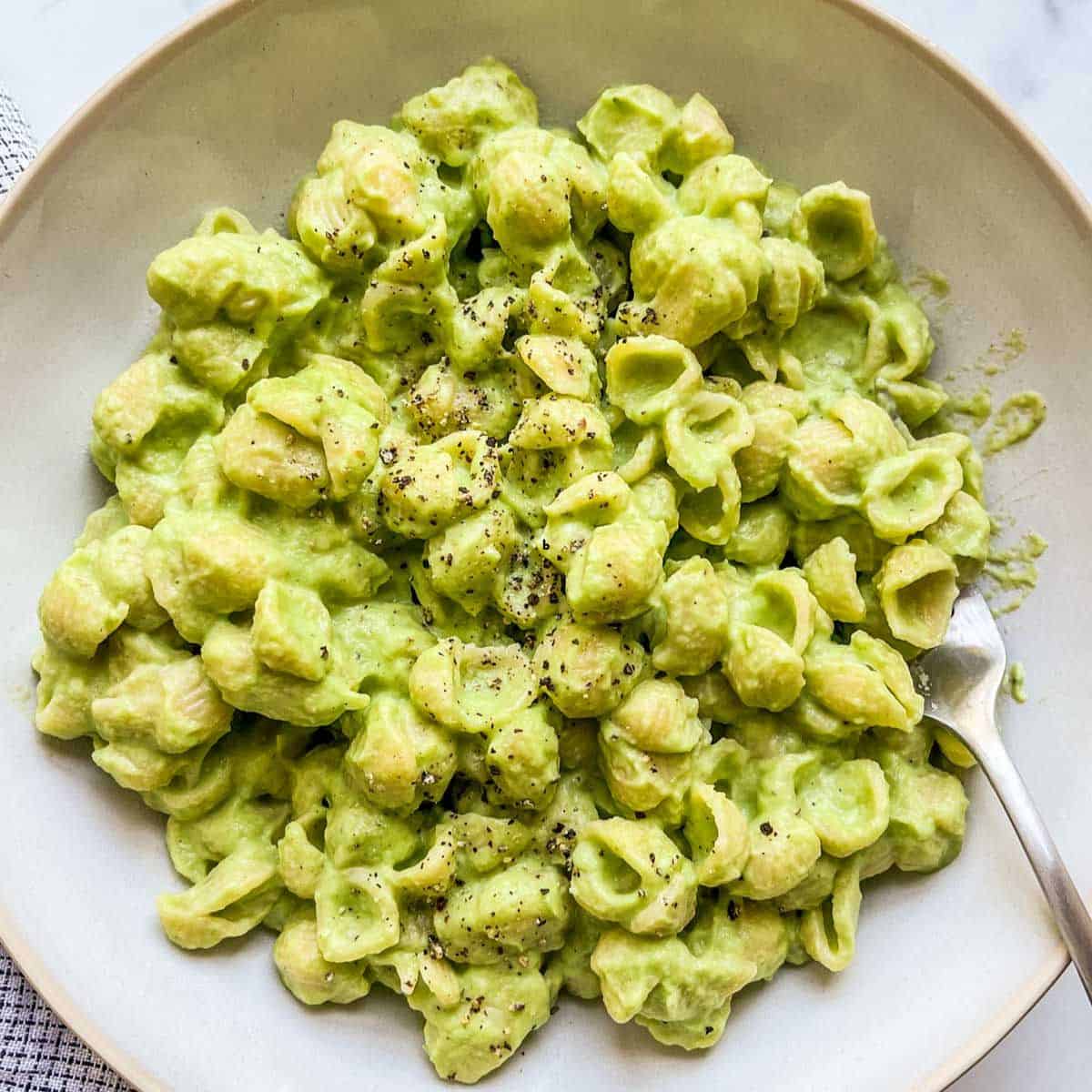Green mac and cheese in a white bowl with a spoon.