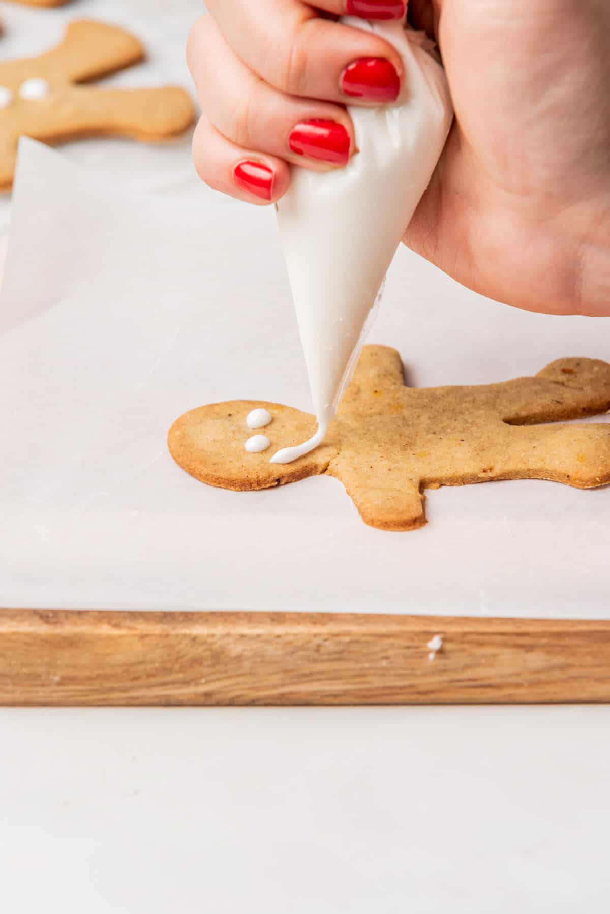 Icing being piped onto a gingerbread man cookie.