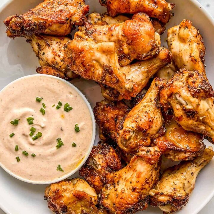 Baked chicken wings with a dipping sauce on a large platter.