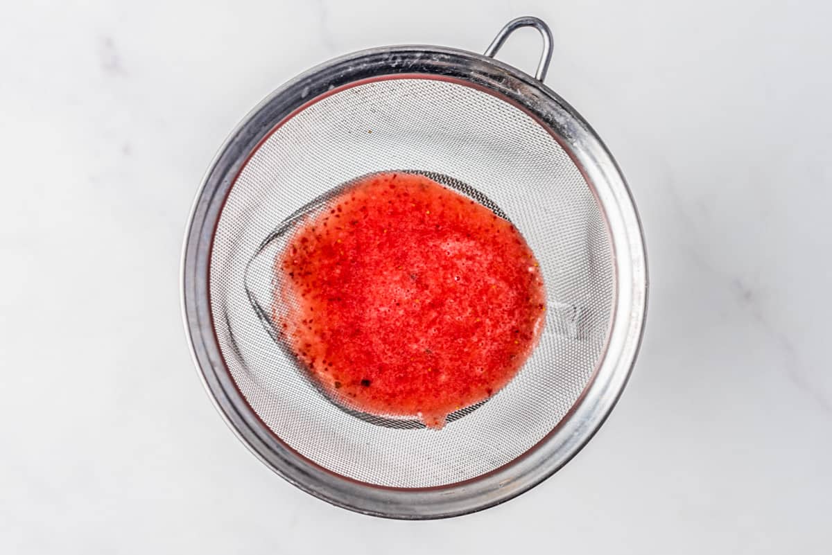 Blended fruit being strained through a sieve.
