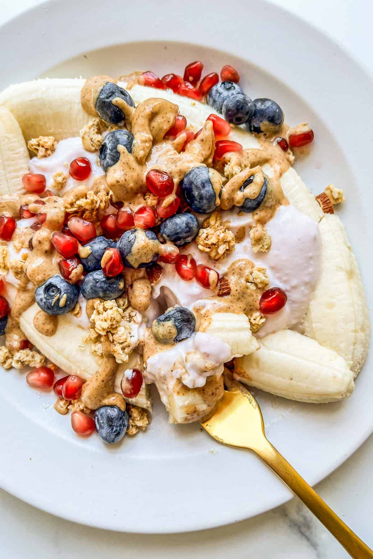 A healthy banana split on a white plate with a gold fork.