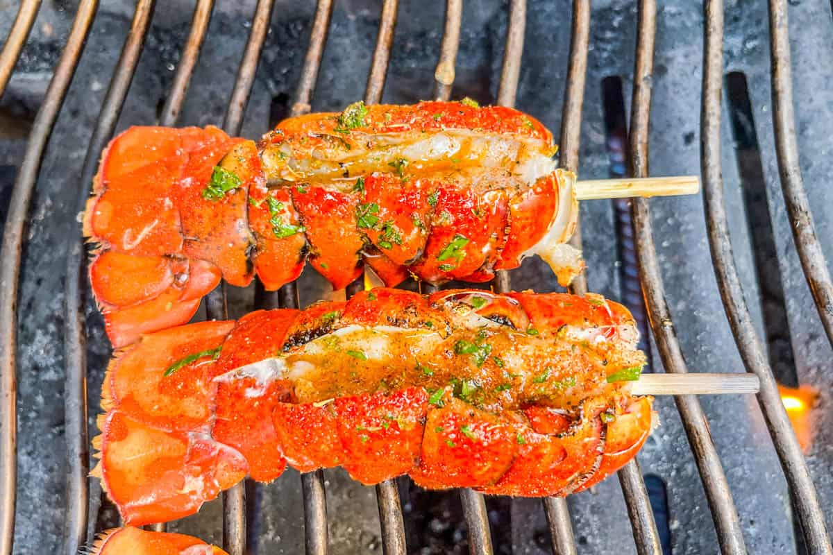 Lobster tails with skewers through them on the grill.