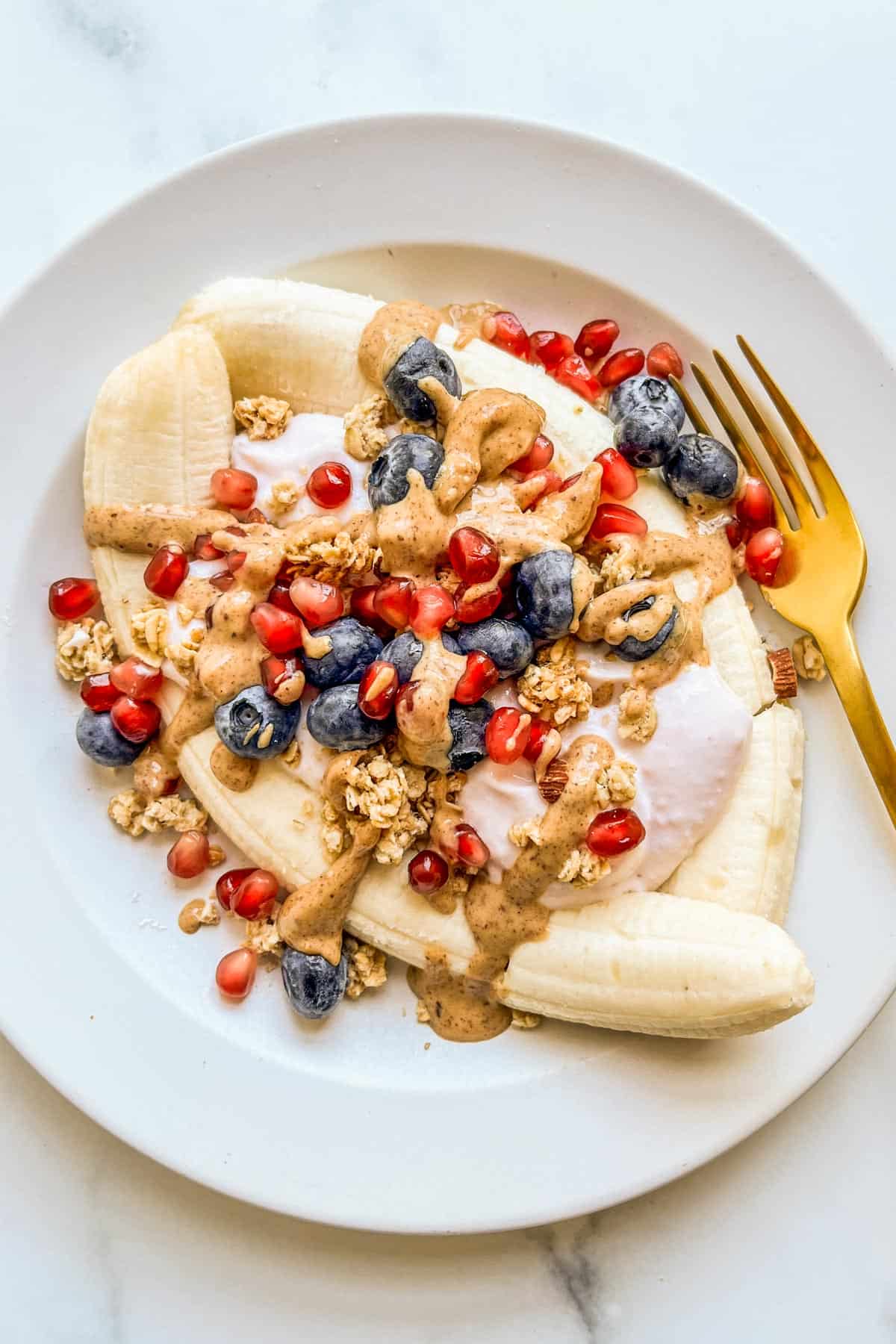 A healthy banana split on a white plate with a gold fork.