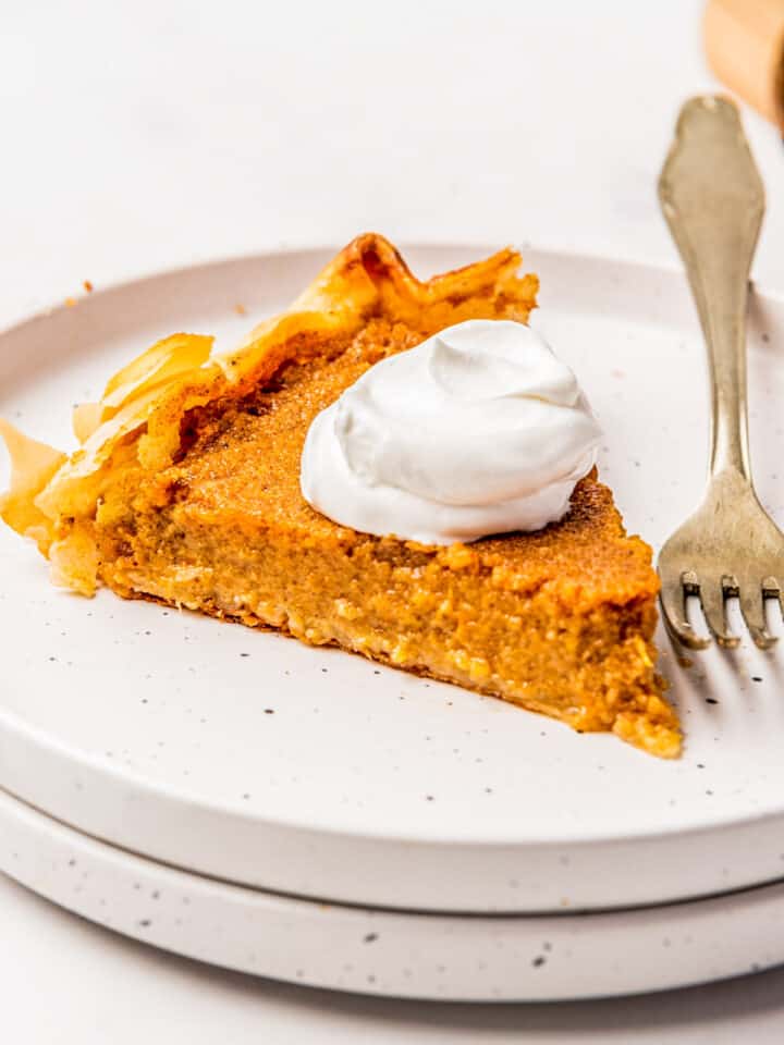 A slice of sweet potato pie on a white plate with a fork.