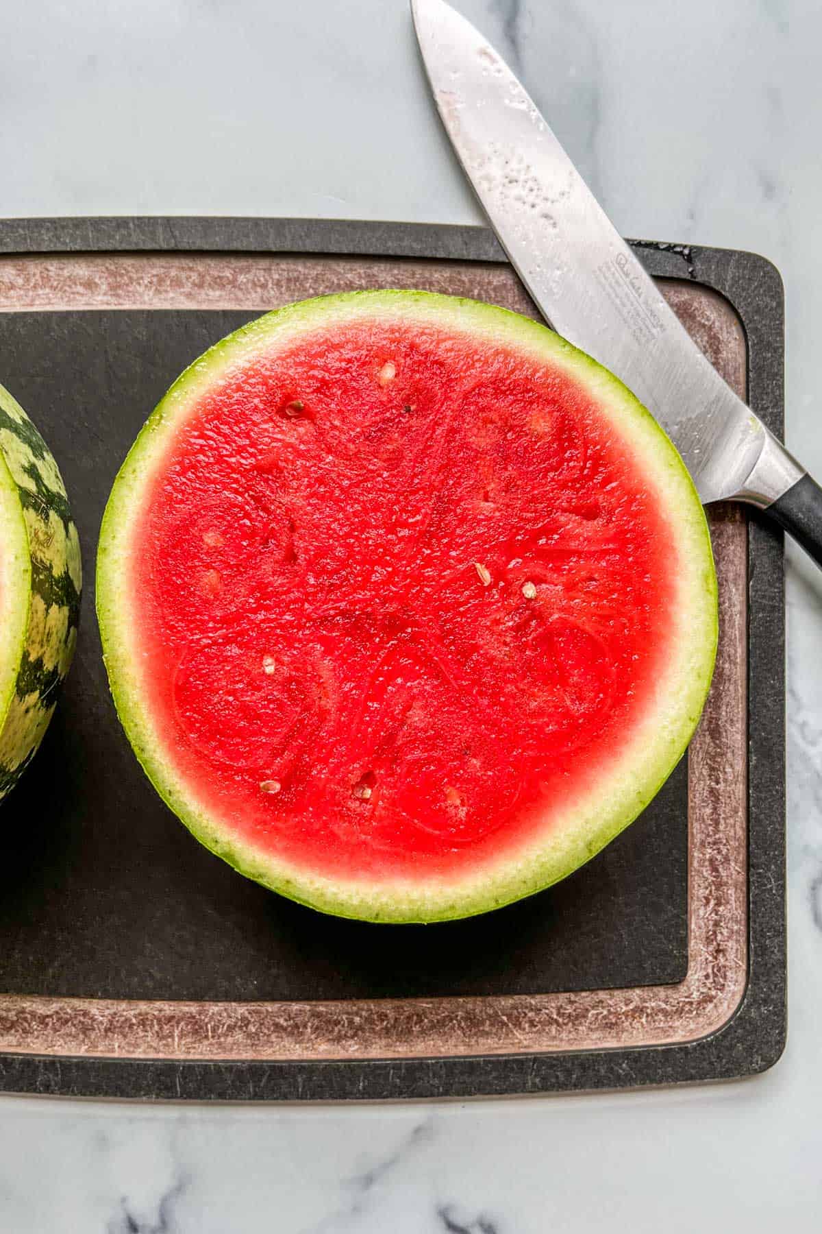A halved mini watermelon on a cutting board.