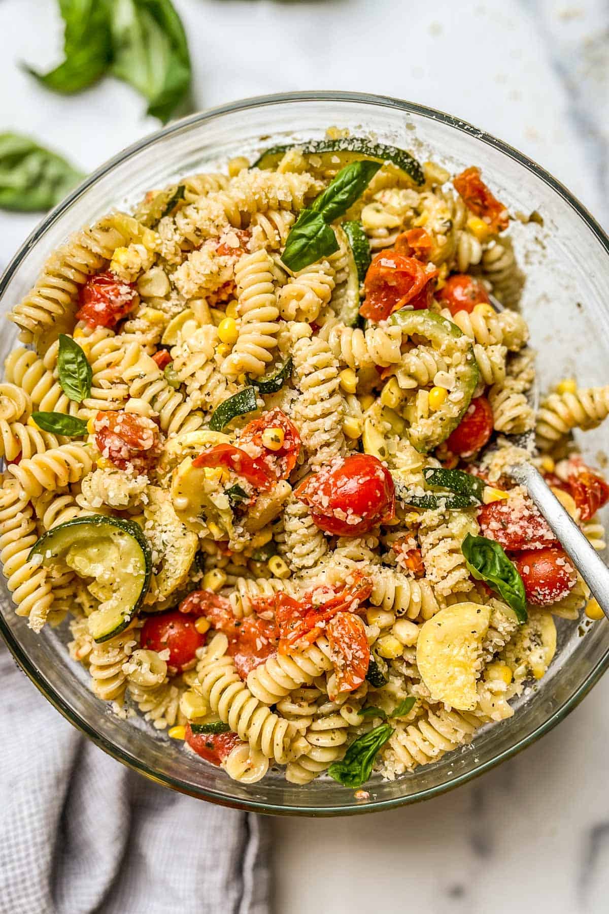 Pesto pasta salad in a glass bowl with a silver spoon.