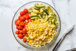 Sweet corn, zucchini, summer squash, and tomatoes in a glass bowl.