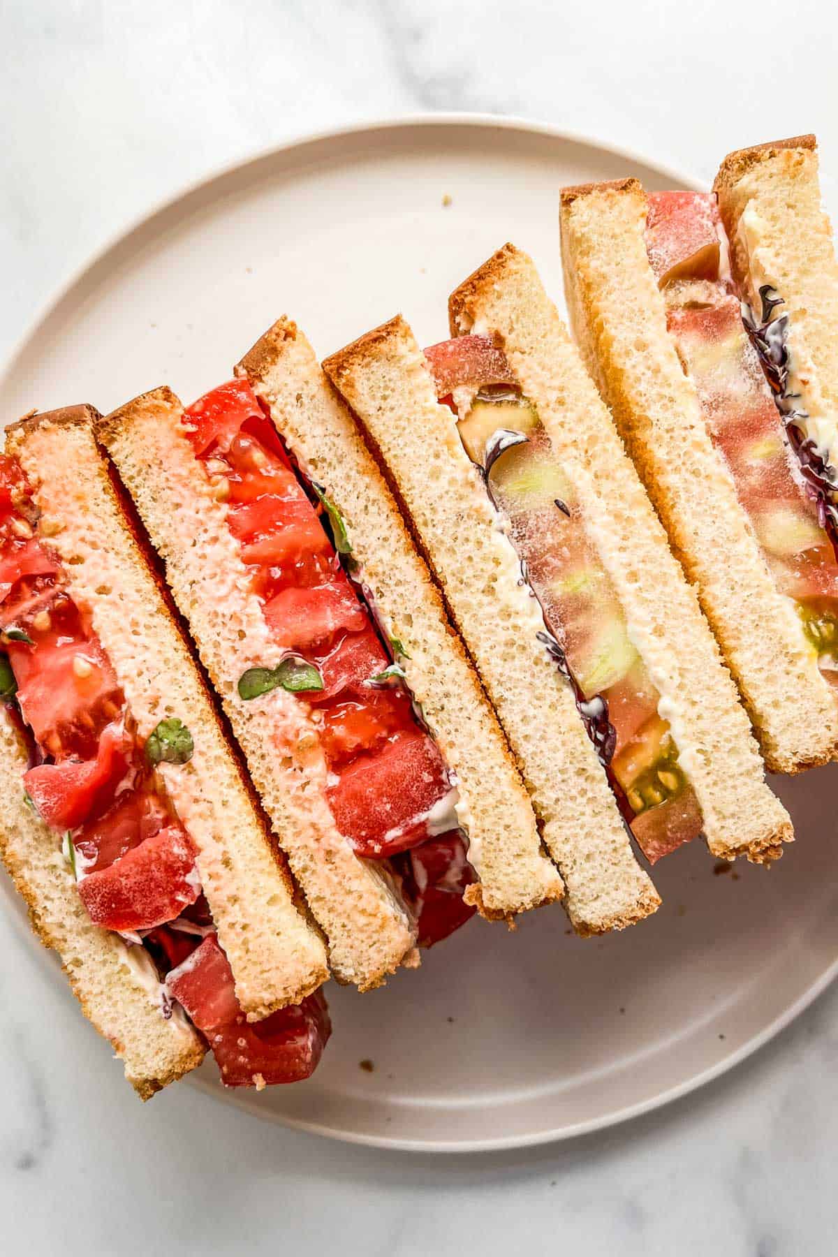 Two tomato sandwiches on a white plate.