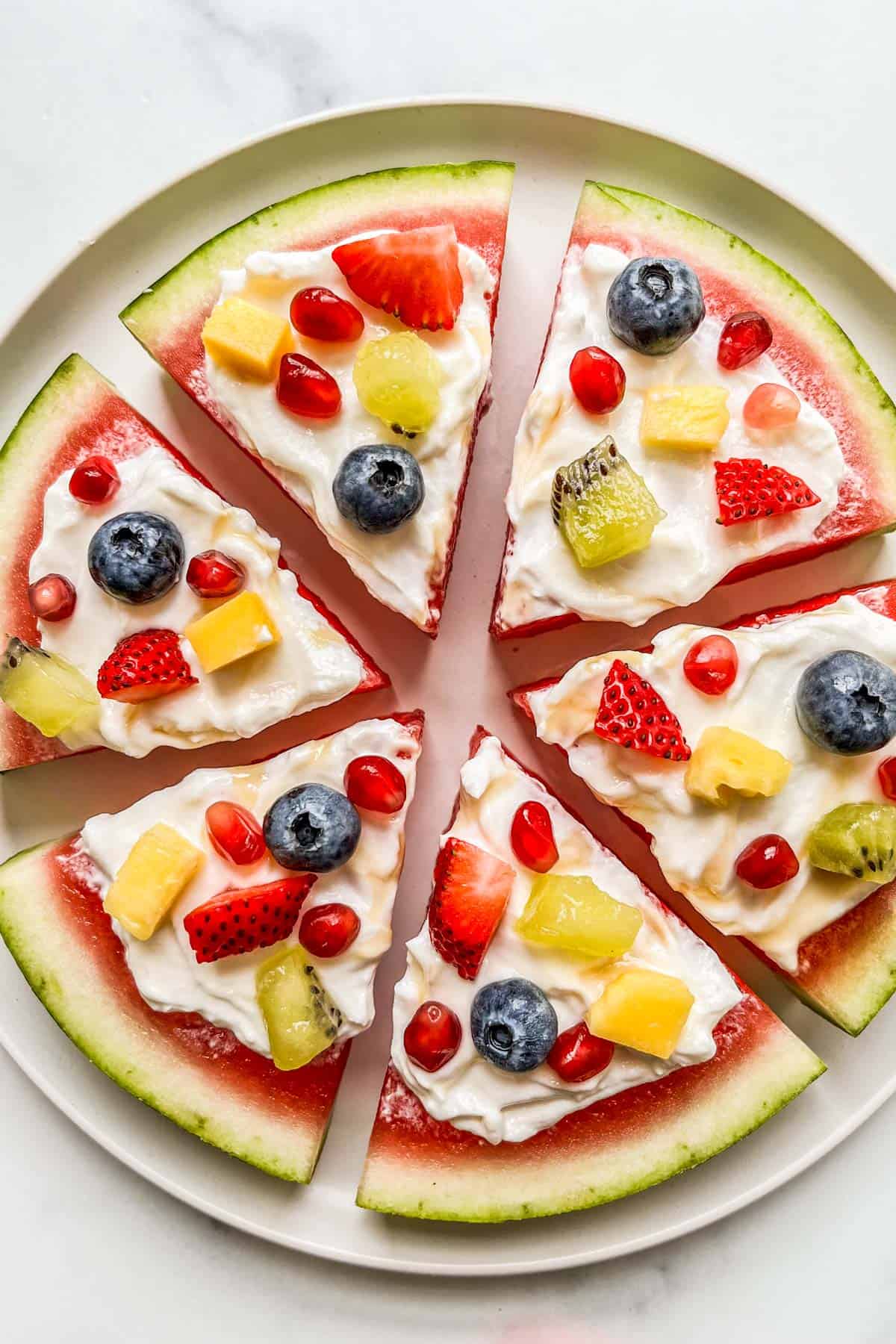 Watermelon pizza with small pieces of fruit and berries on a white plate.