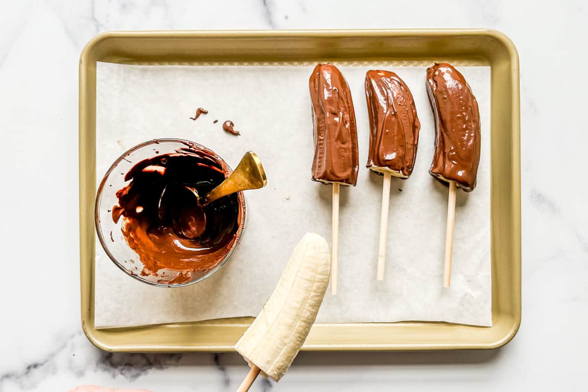 Banana halves on skewers being coated in melted chocolate.