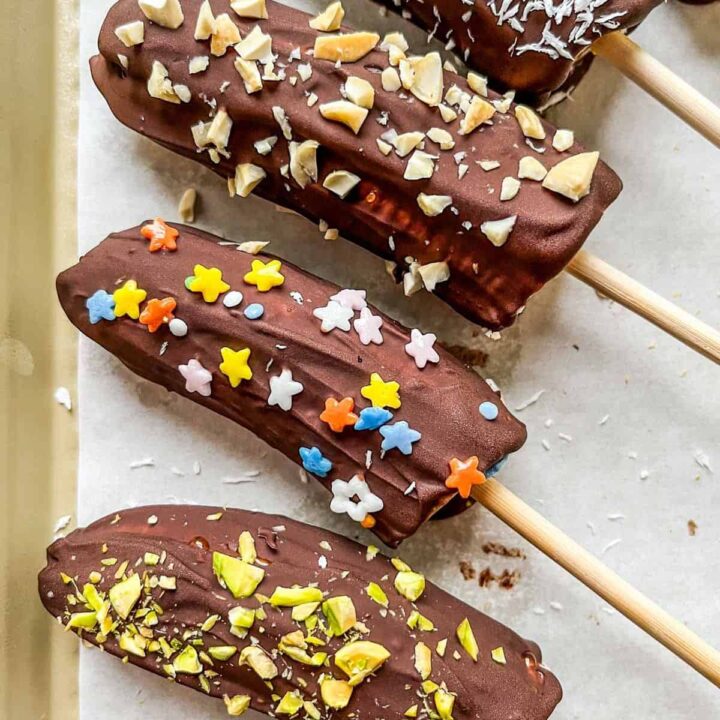 Chocolate covered bananas on a parchment lined baking sheet.