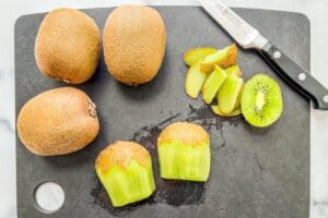 A halved kiwi next to three whole kiwis.