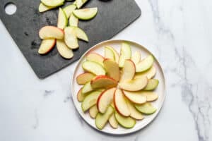 Sliced apples arraigned on a white plate next to a black cutting board with apple slices.