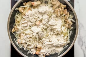 Flour on top of onions and mushrooms in a frying pan.