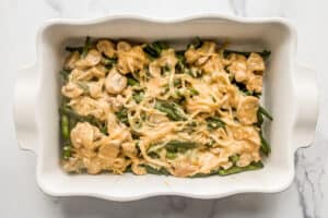 Green bean casserole being assembled in a white casserole dish.