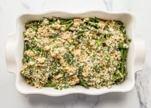 Green bean casserole topped with panko and parmesan in a white dish.