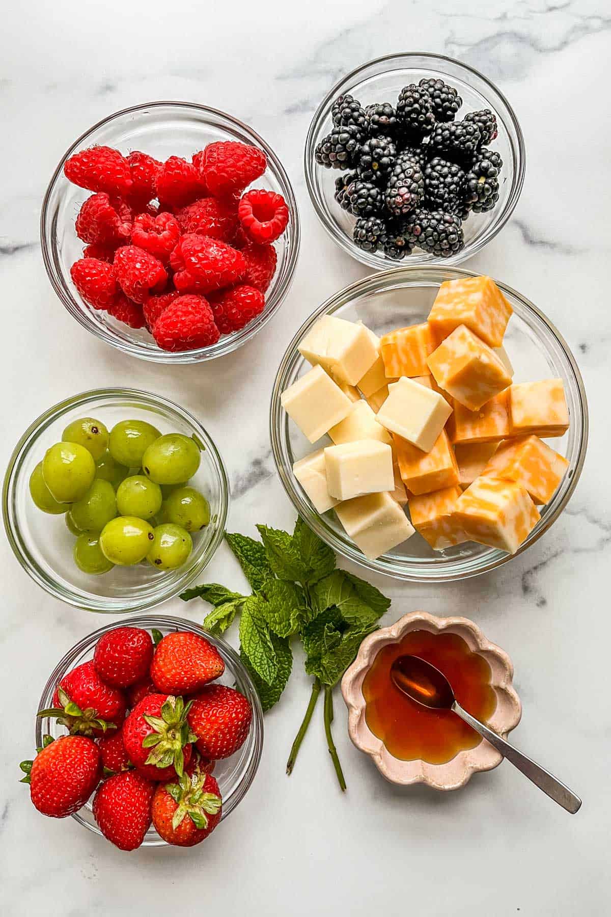 Bowls of berries, fruit, cheese cubes, and honey with some fresh mint.