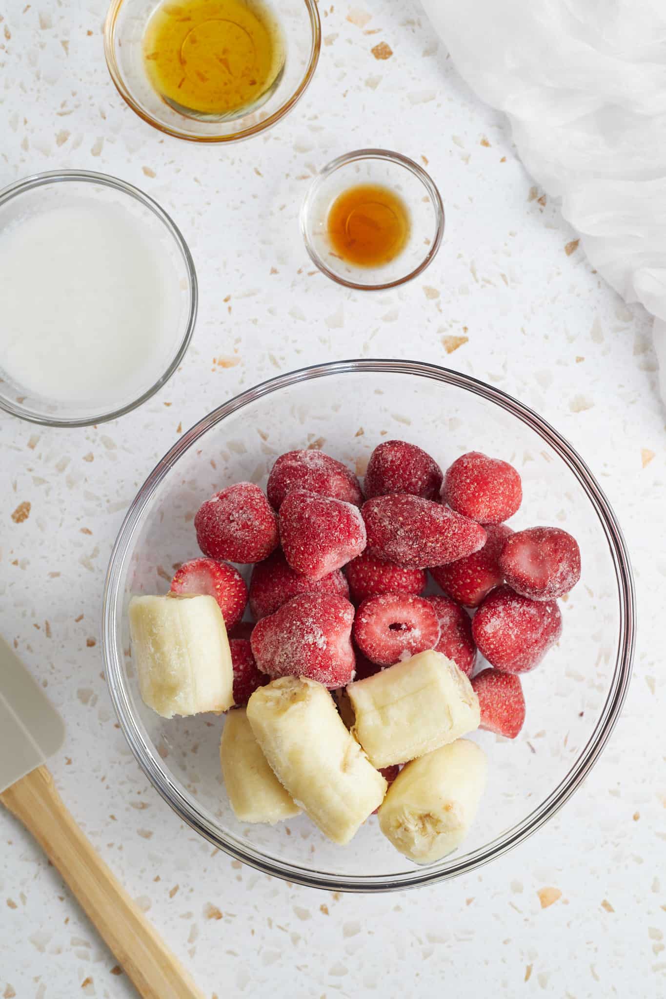 Ingredients for strawberry banana smoothie bowl in glass bowls.