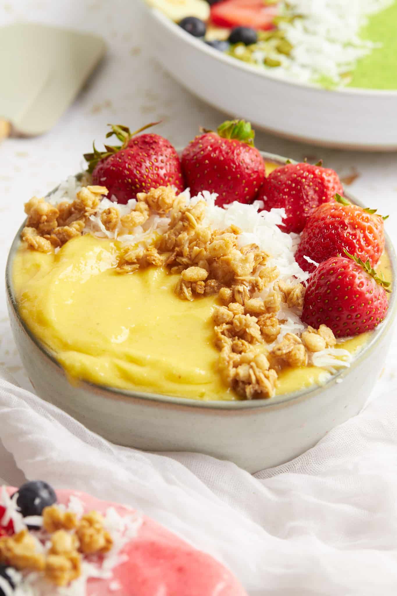 A mango peach smoothie bowl topped with strawberries, coconut, and granola.