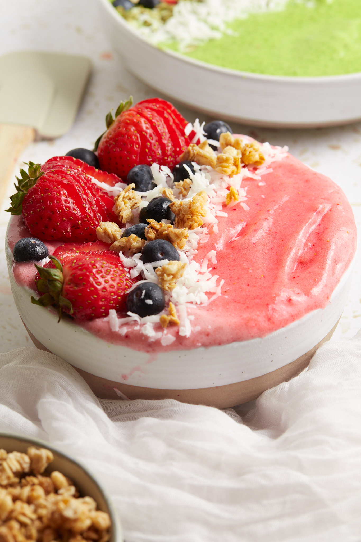 A strawberry banana smoothie bowl topped with strawberries, blueberries, coconut, and nuts.