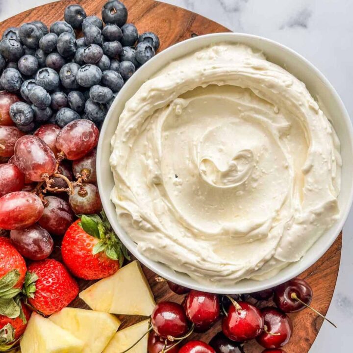 Cream cheese fruit dip in a white bowl on a platter with fruit.