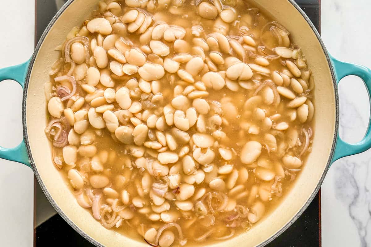 Butter beans with stock, miso, shallots, and garlic in a large pan.