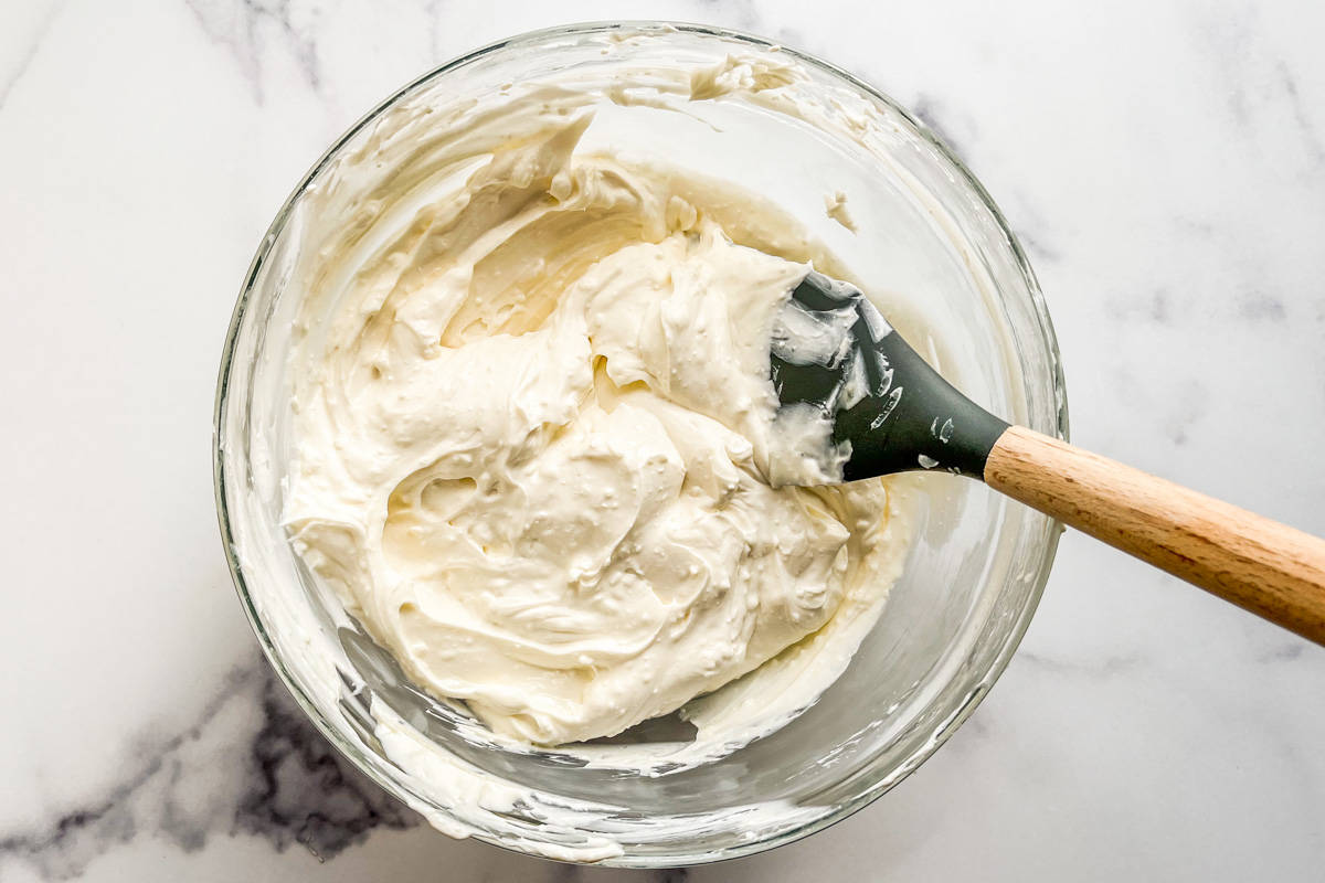 Cream cheese dip being whipped in a glass bowl.