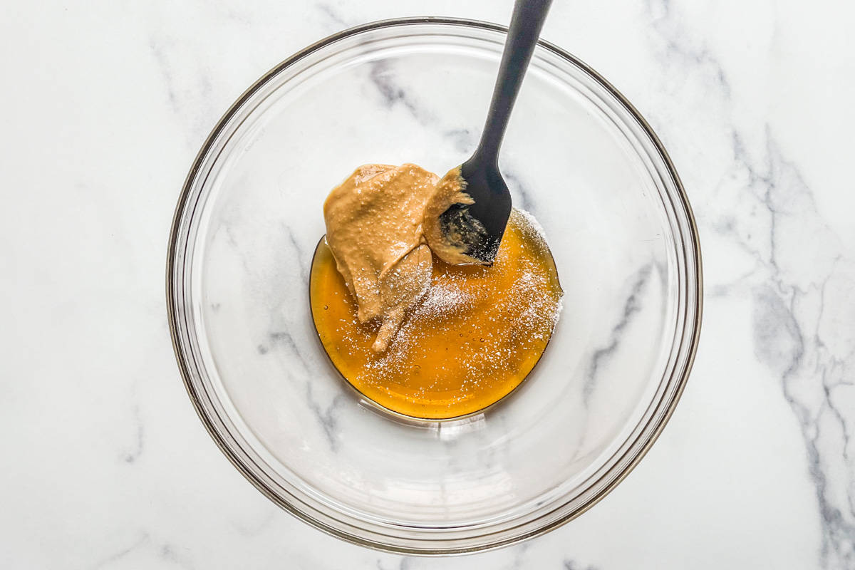 Peanut butter, honey, and salt in a large glass mixing bowl with a black spatula.