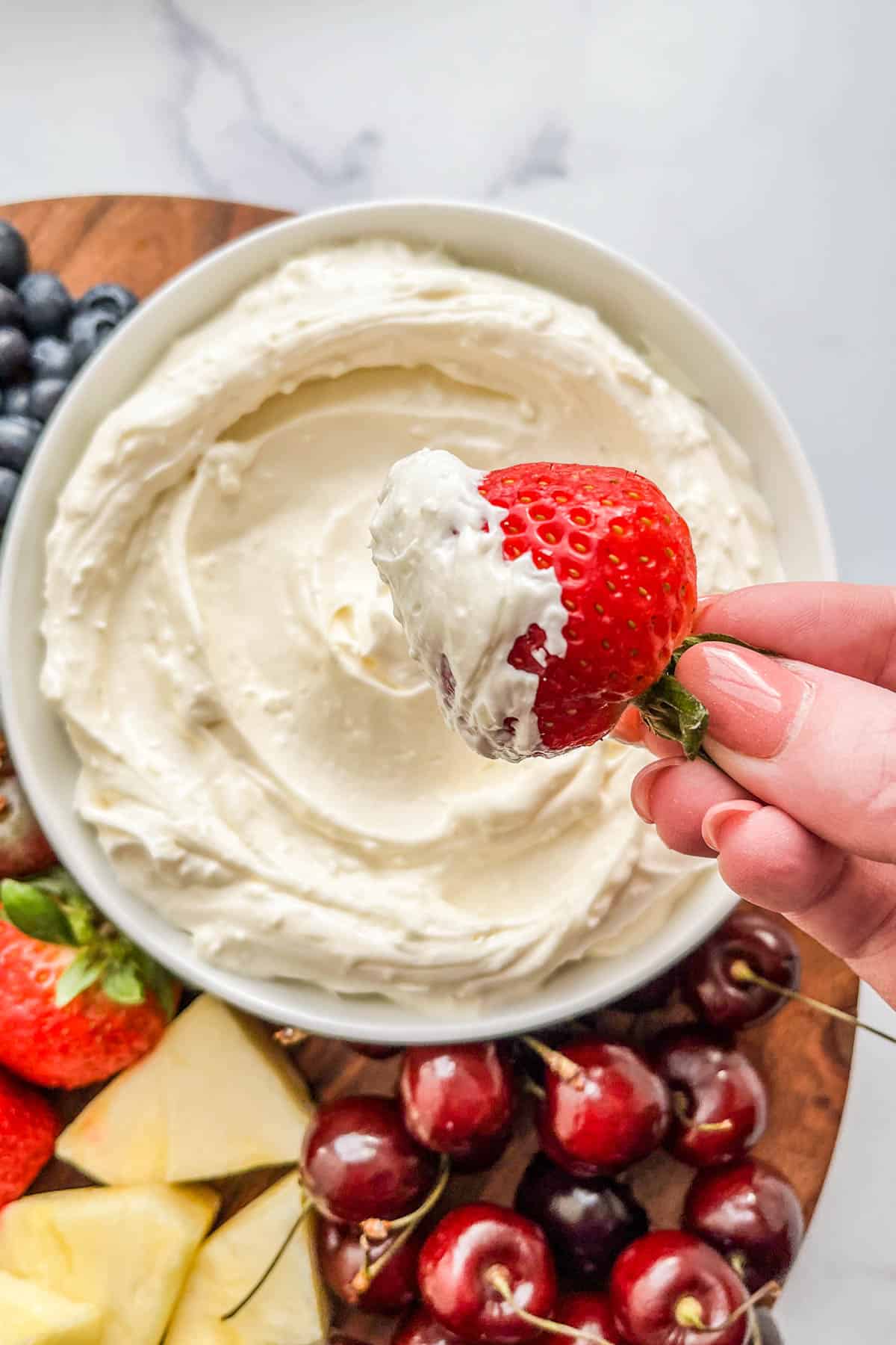 A strawberry being dipped into a cream cheese fruit dip.