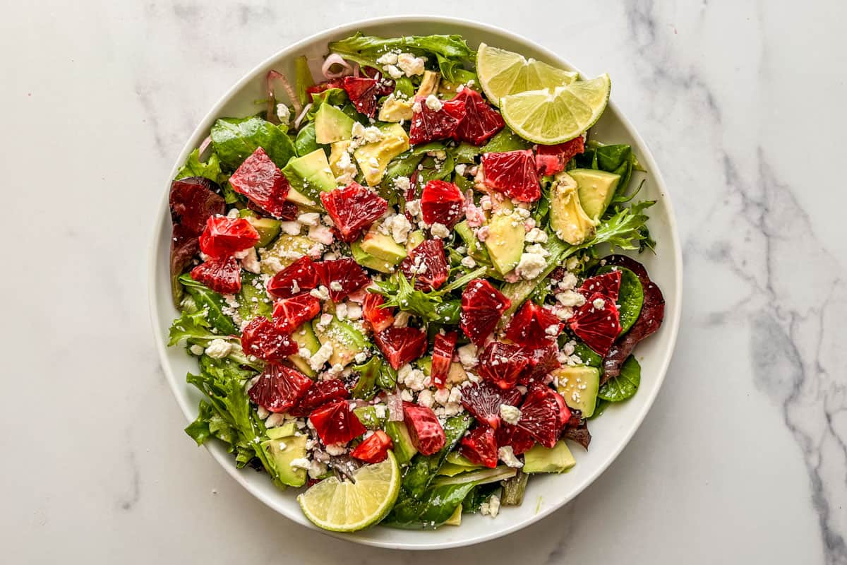 A blood orange salad with avocados, feta, and shallots in a large serving bowl.