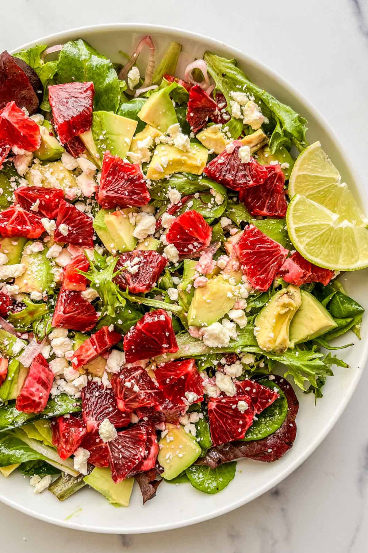 A blood orange salad with avocados and feta in a large white serving bowl.