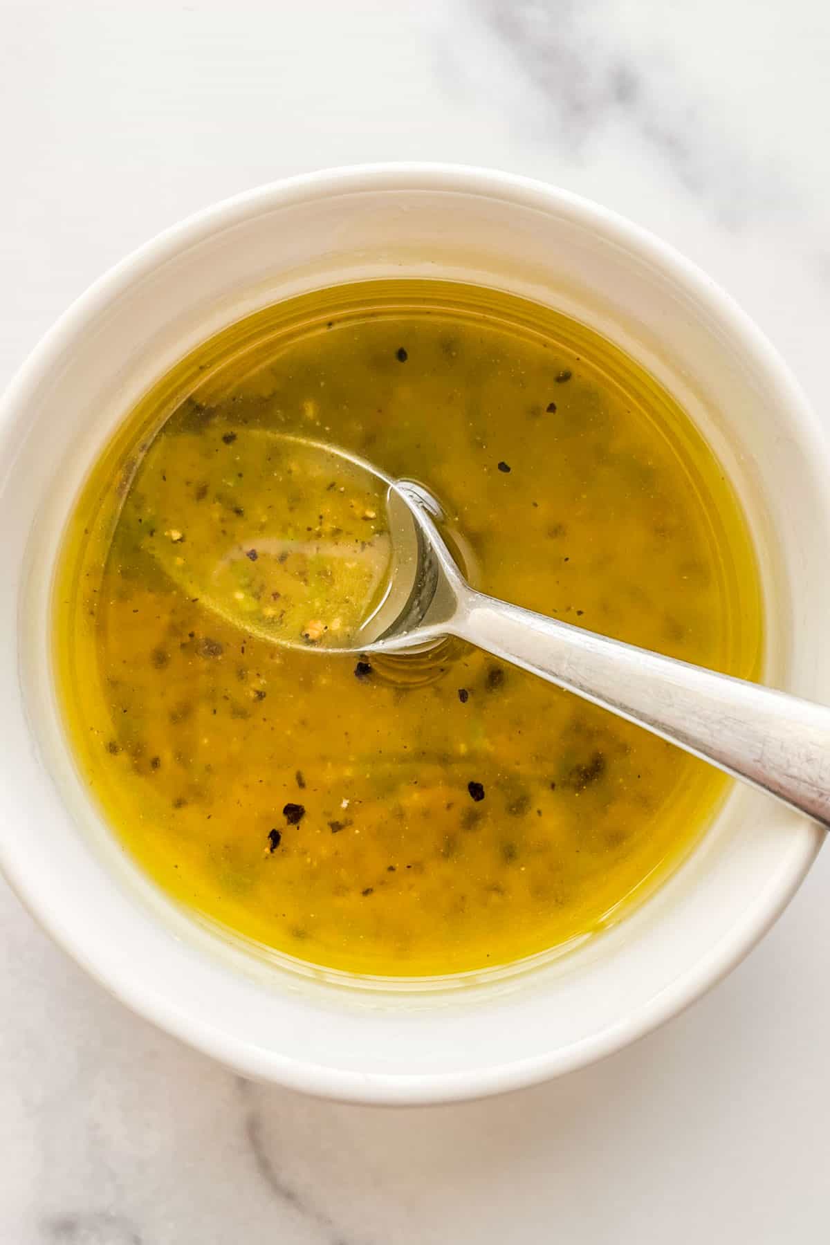 A small white bowl with citrus honey salad dressing with a small silver spoon.