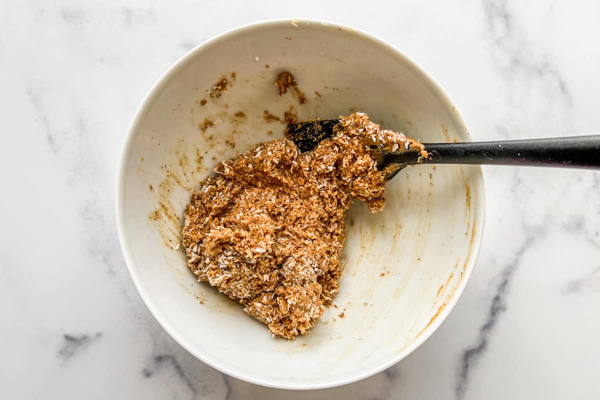 A paste of coconut flakes, almond butter, and maple syrup in a white bowl.