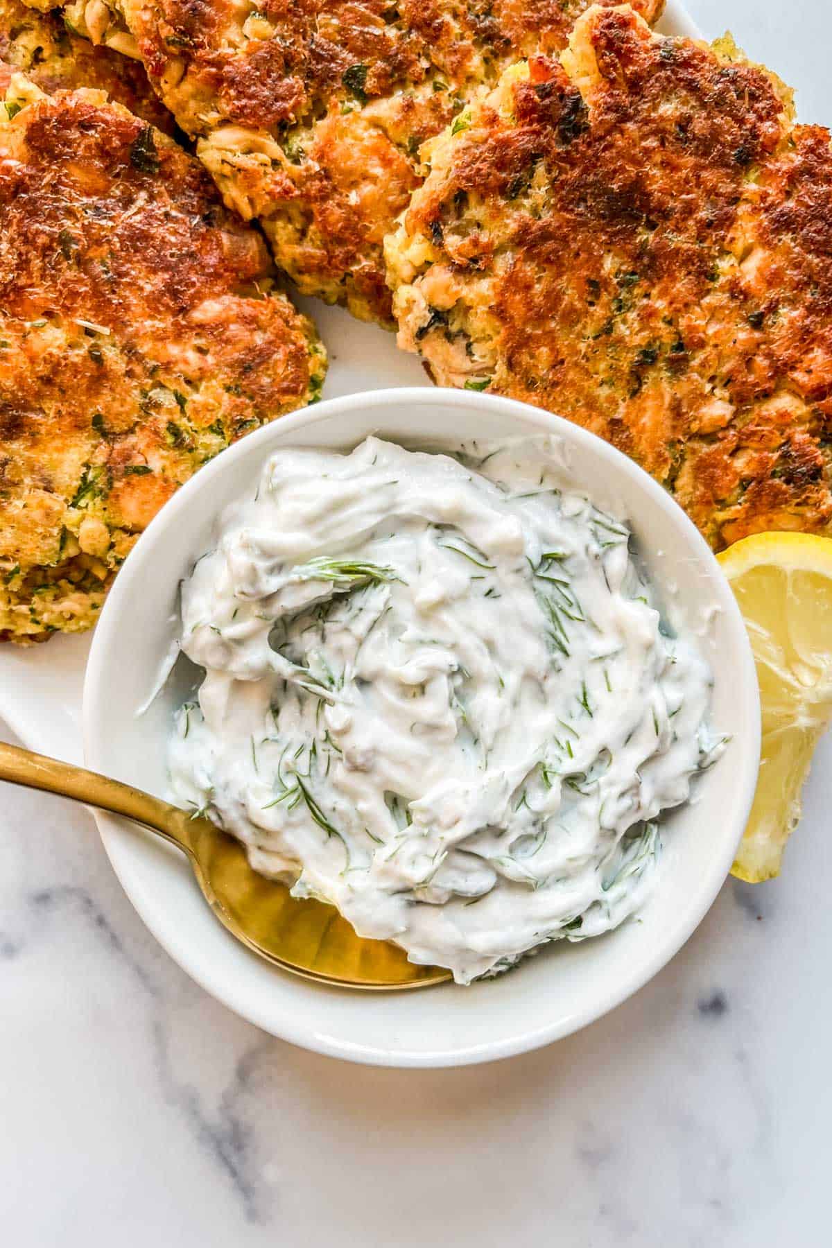Dill sauce in a small white bowl next to salmon patties.