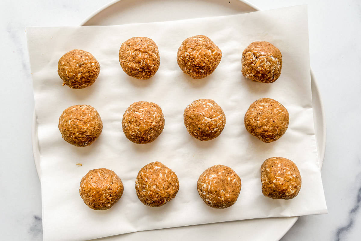 Twelve small balls of coconut and almond butter mixture on a white plate with parchment paper.