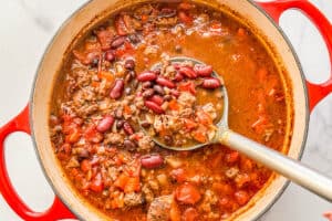 Ground beef chili being ladled out of a dutch oven.