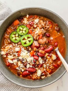 Healthy ground beef chili in a black bowl topped with jalapeños and feta cheese.