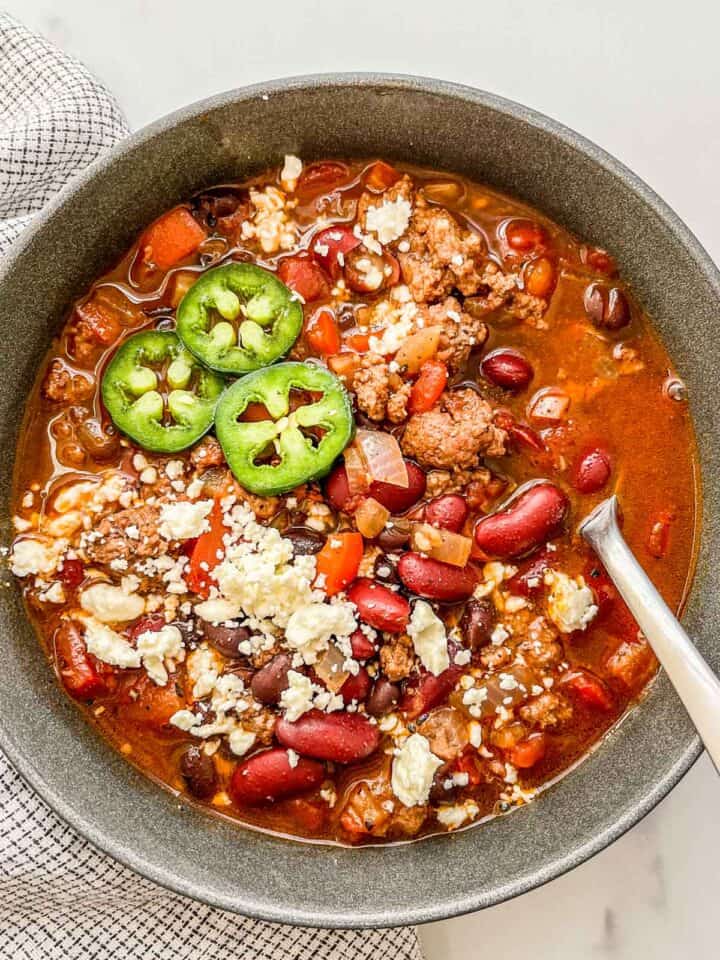 Healthy ground beef chili in a black bowl topped with jalapeños and feta cheese.