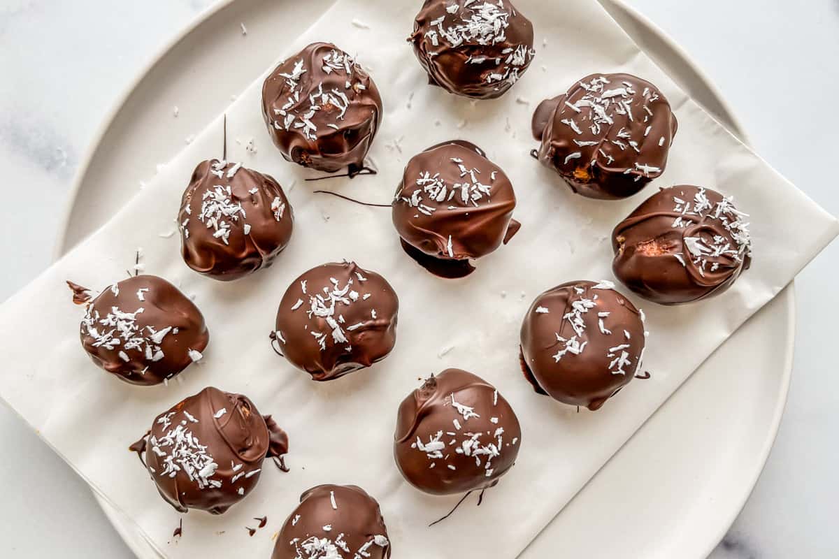 Twelve dark chocolate coconut balls on a piece of parchment paper on a white plate.