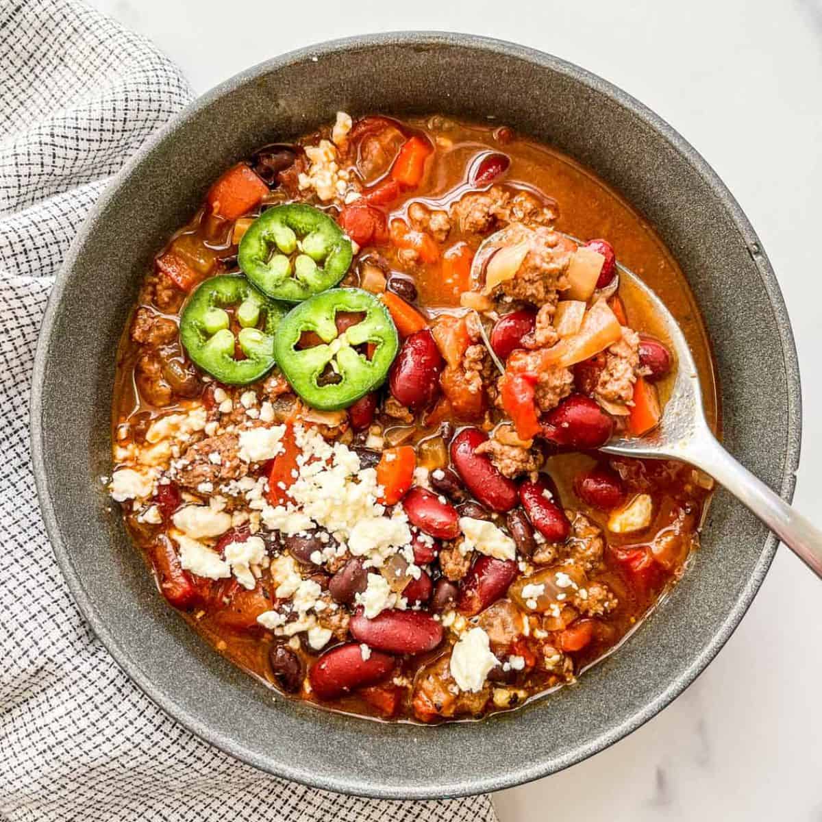 Ground beef chili in a black bowl topped with jalapeños and feta cheese.