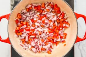 Diced red onion and red bell pepper being cooked in a dutch oven.