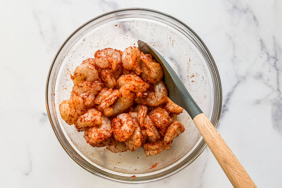 Seasoned shrimp in a glass bowl with a spatula.