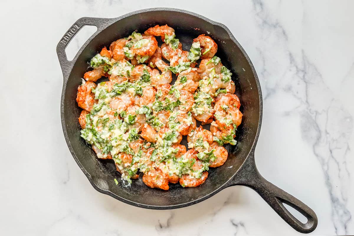 Seasoned shrimp topped with garlic butter parsley sauce in a cast iron pan.